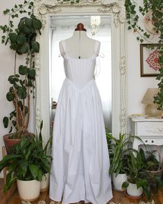 a white dress sitting on top of a wooden floor next to potted plants and a mirror