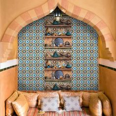 a couch with pillows on it in front of a wall covered in decorative tiles and shelves