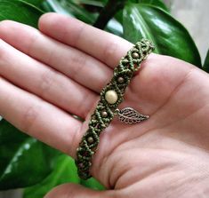 a hand holding a green bracelet with beads and a leaf broochet on it