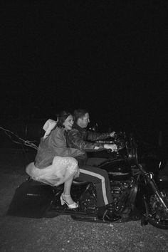 a man and woman riding on the back of a motorcycle at night in the dark