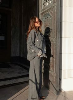 a woman standing in front of a door wearing sunglasses and a suit with long sleeves