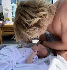 a woman holding a baby in her arms while laying on top of a bed next to another person