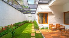 an enclosed patio with wooden benches and green grass on the ground, next to a white building