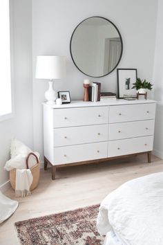 a bedroom with a white dresser and large round mirror on the wall over it's headboard