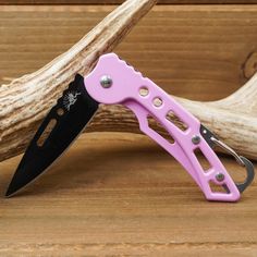 a pink and black knife sitting on top of a wooden table next to a branch