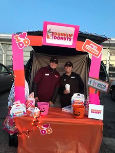 two people standing under a dunkin donuts booth