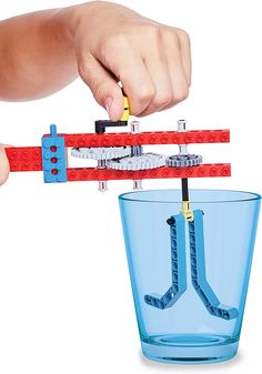 a hand is holding a lego model in front of a glass with water inside it