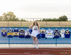 a cheerleader is standing in front of her team's uniforms on the sidelines