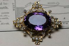 A beautiful  antique Late Victorian to Edwardian 14k yellow gold large  amethyst and seed pearl  brooch.  A lovely design with shamrocks at the four corners and the gold work set with 44 tiny seed pearls.   The brooch measures 1 5/8"  x  1 1/2". There is a large oval faceted amethyst in the center prong set and measures approx. 21mm  x  15mm  x 10mm  (16.7ct).   Set down into the gold are 44 small seed pearls with the size ranging around .75mm to 2.5mm .  The back is fitted with a ball hinge and Elegant Purple Gemstone Brooches, Elegant Amethyst Brooches For Wedding, Purple Gemstone Wedding Brooches, Purple Gemstone Brooches For Weddings, Elegant Purple Brooches For Anniversary, Antique Purple Brooches For Formal Occasions, Elegant Gold Amethyst Brooches, Antique Purple Formal Brooches, Purple Victorian Wedding Brooches