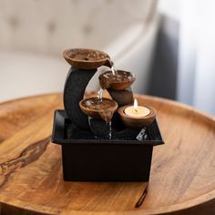 a wooden table topped with three candles on top of a black square container filled with water