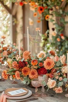 an arrangement of flowers and candles on a wooden table with oranges, yellows and pinks