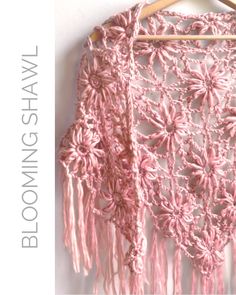 a pink crocheted shawl hanging on a wooden hanger next to a white wall