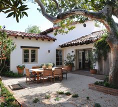 an outdoor dining area in front of a white house with potted plants on the patio