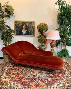 a red couch sitting on top of a rug next to a lamp and potted plants