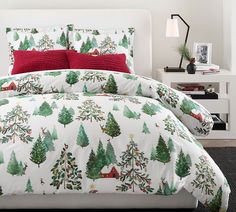 a bed with christmas trees on it and red pillows in the corner next to a nightstand