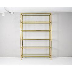 a gold metal shelf with three shelves on each side and two white walls in the background