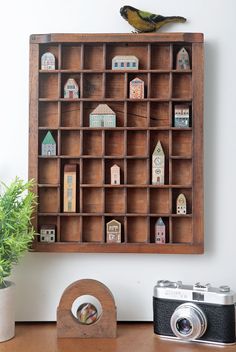 a wooden shelf filled with miniature houses on top of a table next to a potted plant