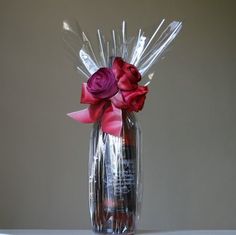 a clear vase filled with red and pink flowers on top of a table next to a wall