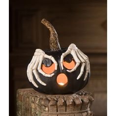 a black pumpkin with white hands and orange eyes is sitting on top of a piece of wood