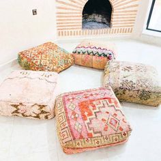 four colorful poufles sitting on the floor in front of a brick oven and window