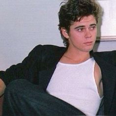 a young man sitting on top of a couch wearing a white shirt and black blazer