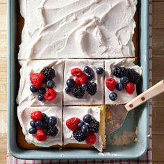 a cake with white frosting and berries on top is in a blue pan next to a spatula