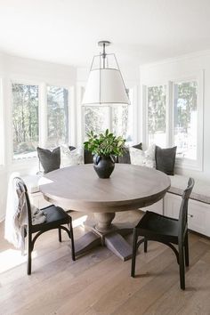 a dining room table with two chairs and a vase on top of it in front of some windows