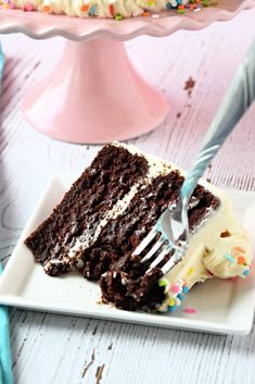 a slice of chocolate cake with white frosting and sprinkles on a plate