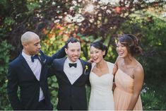 a group of people standing next to each other in front of trees and bushes with their arms around one another