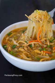 a white bowl filled with noodles and carrots on top of a black table next to a spoon