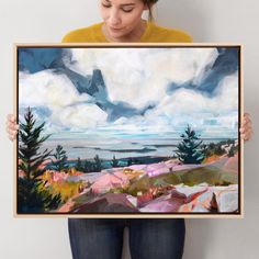 a woman holding up a painting in front of her face with clouds and mountains in the background