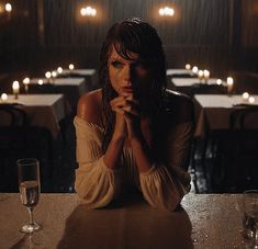 a woman sitting at a table with her hands folded in front of her face and candles behind her