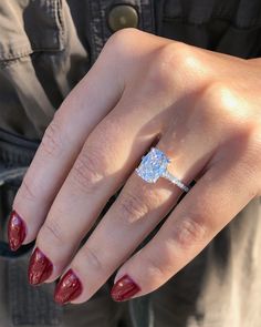 a woman's hand with red fingernails and a ring on her finger, holding an engagement ring