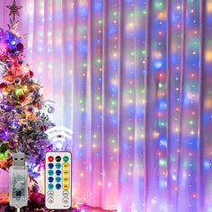 a christmas tree and remote control in front of a curtained window with lights on it