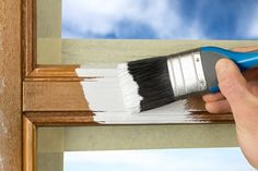 a person holding a paint brush over a window frame with sky in the back ground