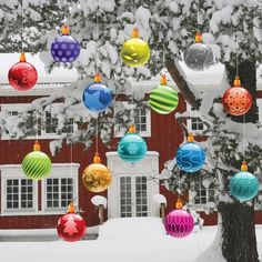 christmas ornaments hanging from a tree in front of a red house with snow on the ground