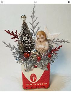 a tin can filled with christmas decorations on top of a white table next to a tree