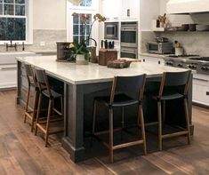 a large kitchen island with four chairs around it and an oven in the back ground