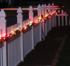 a white picket fence with christmas lights on the top and bottom, along side it