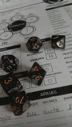 black and gold dice sitting on top of a table next to some papers with numbers