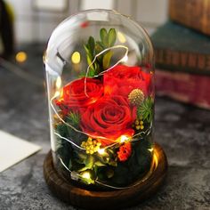 a glass dome with red roses and greenery in it on top of a table