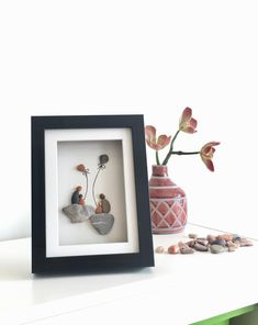 a vase with flowers and rocks in it next to a photo frame on a table