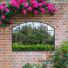 a brick wall with a window that has pink flowers growing on it and some bushes in the background