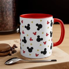 a red and white mickey mouse mug sitting on top of a wooden table next to a cookie