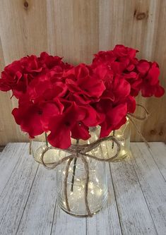 a glass vase filled with red flowers sitting on top of a white wooden table next to a wall