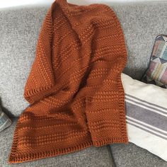 an orange knitted sweater laying on top of a couch next to pillows and a pillow