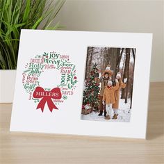 a white photo frame with a christmas tree and two children in the background, on a wooden table