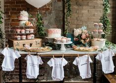 a table with cake, cupcakes and baby onesuits on clothes line