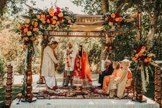 a couple getting married in front of an outdoor wedding ceremony with orange flowers and greenery