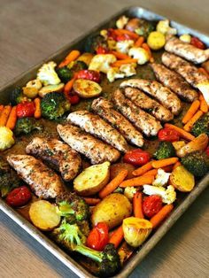 a pan filled with chicken and vegetables on top of a wooden table